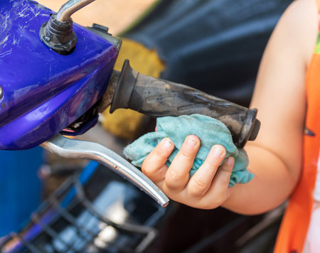 Girl's hand washing a motorbike to help the familyの写真素材