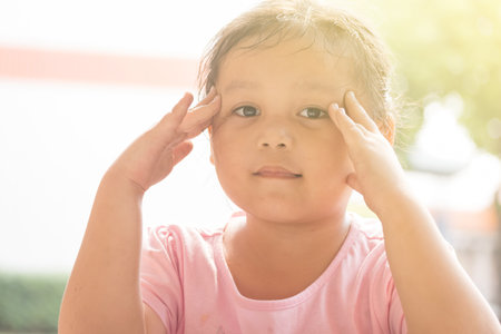 A close up picture of a cute young Asian girl holding up her face with her handsの写真素材