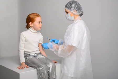 Vaccination of children. A woman doctor makes injection with a syringe of vaccine to a teenage redhead girlの写真素材