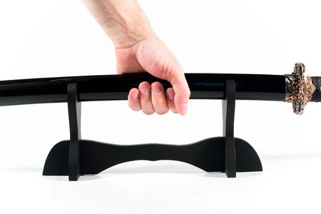 Hand holding a Japanese sword in the sheath (on the wooden tabletop stand)の写真素材