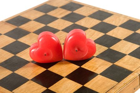 Two heart-shaped red candles on an old chessboardの写真素材