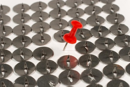 Single red pushpin among sharp steel thumbtacksの写真素材