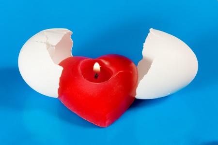 Burning red heart-shaped candle in broken eggshell (symbolizing the Birth of Love)の写真素材