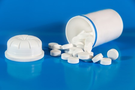 Pill bottle and scattered white pills (on a bright blue background)の写真素材