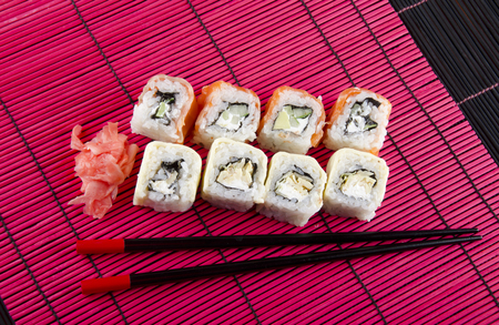 Sushi rolls, ginger and chopsticks on a red and black bamboo backgroundの写真素材