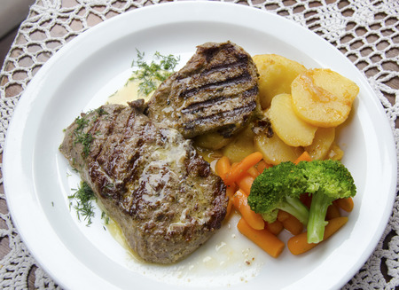 Grilled beef steaks on a plate with potatoes, baby carrots and broccoliの写真素材