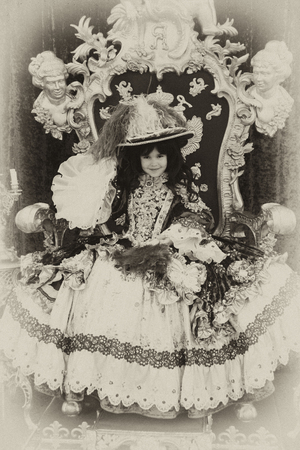 Smiling little girl wearing an antique princess dress sitting on a princess throne, vintage style
