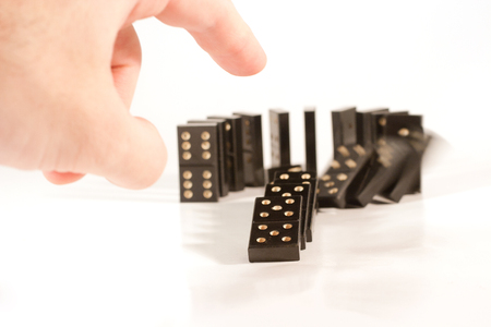 Human hand pushing a row of black dominoes (shallow DOF, selective focus on the finger and domino piece in front of the row)の写真素材