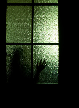 Blurred silhouette of a child behind a glass door in the darknessの写真素材