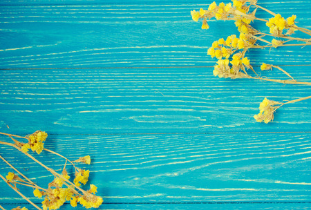 Dry yellow flowers forming a frame on a vintage wooden background, retro style (with copy space in the center for your text)の写真素材