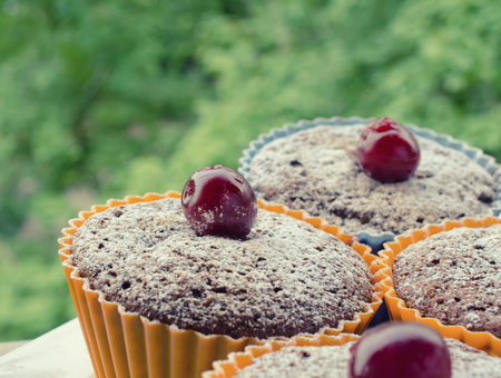 Freshly baked homemade chocolate muffins decorated with cherries and powdered sugar (outdoor picnic or breakfast concept), retro styleの写真素材