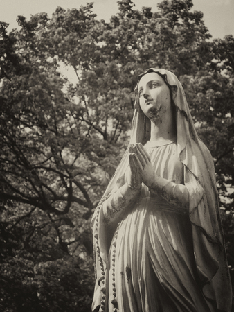 Sad statue among trees in an abandoned ancient cemetery (in sepia, retro style)の写真素材