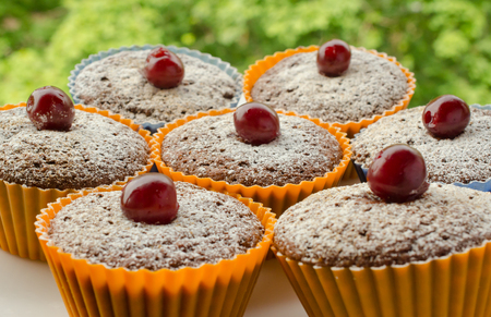 Freshly baked homemade chocolate muffins decorated with cherries and powdered sugar (outdoor picnic or breakfast concept)の写真素材