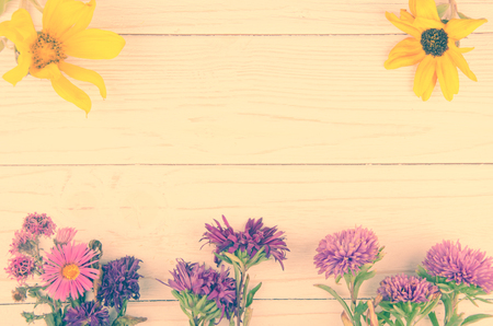 Pink and yellow autumn flowers forming a frame on a wooden background (faded film effect, vintage style), copy space in the center for your textの写真素材