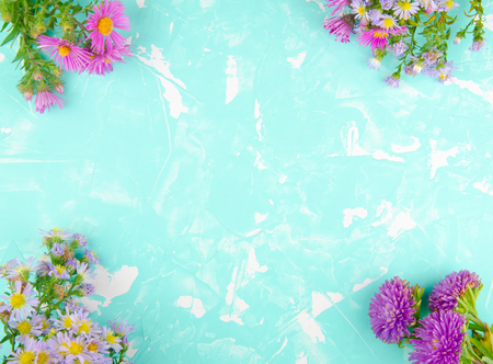 Bouquets of bright violet and purple flowers forming a frame on a turquoise cracked concrete background (with copy space in the center for your text), top viewの写真素材