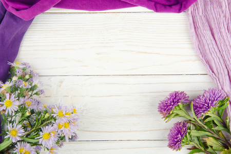 Bouquets of bright violet flowers and pile of scarves forming a frame on a white wooden background (with copy space in the center for your text), selective focus, retro styleの写真素材