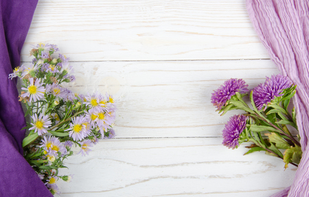 Bouquets of bright violet flowers and scarves forming a frame on a white wooden background (with copy space in the center for your text)の写真素材