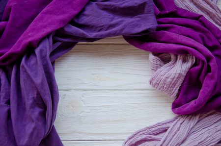 Pile of cozy bright scarves forming a frame on a white wooden background, selective focus (copy space in the center for your text)の写真素材