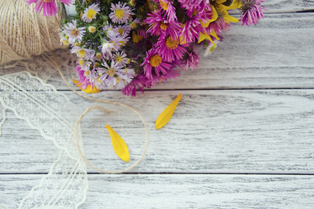 Bright purple and yellow autumn flowers and petals, a spool of thread and lace on a wooden background (with copy space on the right, selective focus on the flowers) as a rustic background, retro styleの写真素材