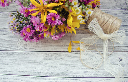 Bouquet of bright purple and yellow autumn flowers, a spool of thread and a bow made of a lace ribbon on a gray wooden background (with copy space for your text, selective focus) as a rustic background, retro styleの写真素材
