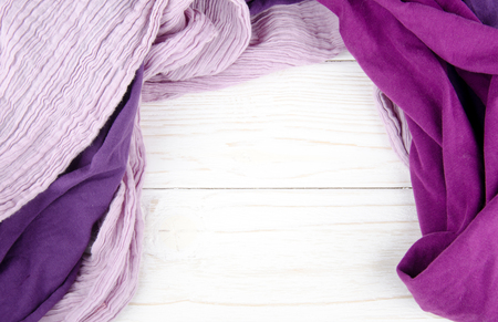 Pile of cozy bright scarves forming a frame on a white wooden background (copy space in the center for your text)の写真素材
