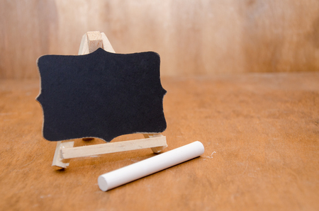 Little blackboard and a piece of white chalk on a worn wooden background (with copy space for your text)の写真素材