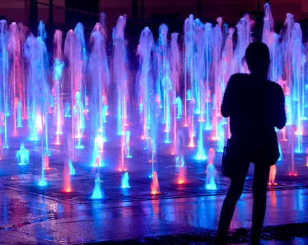 Blurred out-of-focus silhouette of a tourist watching beautiful multicolored dancing fountains at nightの写真素材
