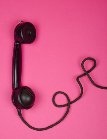 Vintage phone receiver with a cord on a bright pink background, (minimal concept, top view), with copy space for your textの写真素材