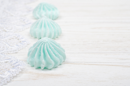 Freshly baked meringue cookies of mint color (on a white wooden background decorated with white lace), shallow DOF, selective focus, copy space on the rightの写真素材