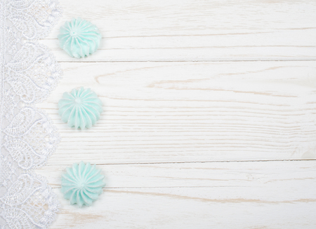 Freshly baked meringue cookies of mint color (on a white wooden background decorated with white lace), top view, copy space on the rightの写真素材