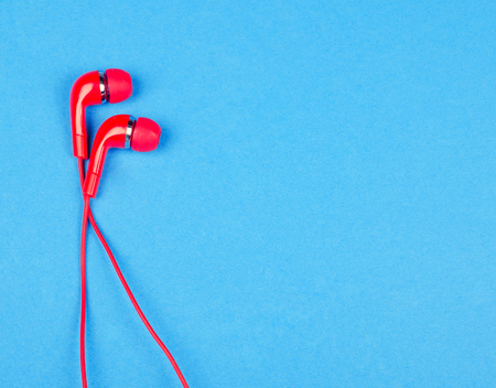 Bright red earbud headphones isolated on a bright blue background with copy space on the right for your text (minimal concept, top view)の写真素材