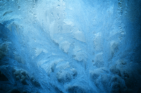 Fantastic fairy-like dark blue frost pattern on the window glass (as an abstract winter background)の写真素材