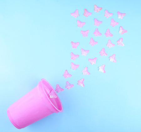 Beautiful pink artificial butterflies flying out of a pink plastic glass (on a blue paper background), minimal concept, flat layの写真素材