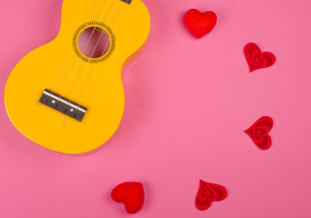 Body of a bright yellow ukulele guitar and red hearts forming a circle against a bright pink background (Love Song concept), copy space in the center for your textの写真素材