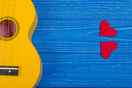 Body of a bright yellow ukulele guitar and red hearts against a bright blue wooden background (Love Song concept)の写真素材