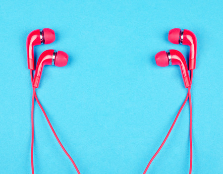 Two pairs of bright red earbud headphones isolated on a bright blue background (minimal concept, top view), copy space in the center for your textの写真素材