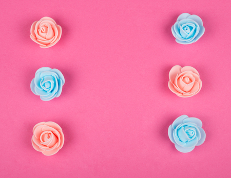 Handmade rose buds of pink and blue colors forming a frame on a pink background (minimal concept, top view), copy space in the center for your textの写真素材