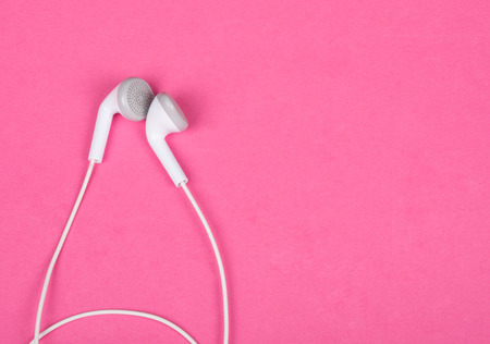 White earbud headphones isolated on a pink background with copy space on the right for your text (minimal concept, top view)の写真素材