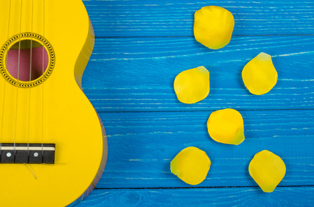 Body of a bright yellow ukulele guitar and petals of bright yellow handmade roses against a bright...