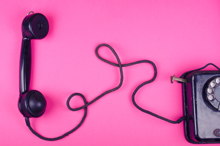 Black vintage phone and a receiver with a cord on a pink background, retro toned (minimal concept, top view)の写真素材