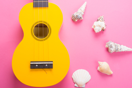 Body of a bright yellow ukulele guitar and seashells on a pink background (as a tropical vacation concept)の写真素材