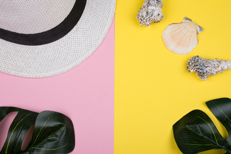 White hat, monstera leaves and seashells on pink and yellow backgrounds (top view, tropical vacation concept)の写真素材