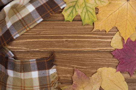 Cozy checkered scarf and autumn leaves on a wooden background, top viewの写真素材