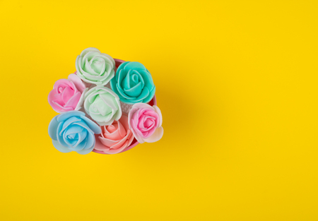 Bunch of multicolored handmade rose buds in a pink bucket on a bright yellow backgroundの写真素材