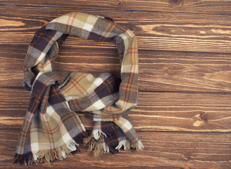 Cozy checkered scarf on a brown wooden background, top view (copy space on the right), retro styleの写真素材