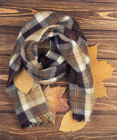 Cozy checkered scarf and autumn leaves on a wooden background, top viewの写真素材
