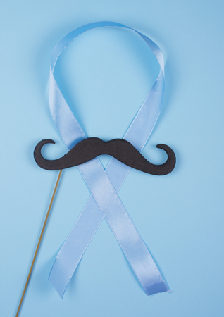 Black moustache on a wooden stick and a blue ribbon as a symbol of the anti-cancer campaign (on a blue background)の写真素材