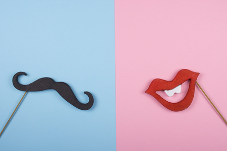Moustache and a red mouth on wooden sticks against a split blue and pink background (copy space for your text) as the male and female conceptの写真素材