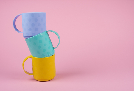 Stack of blue, green and yellow cups on a pastel pink background (minimalism concept)の写真素材