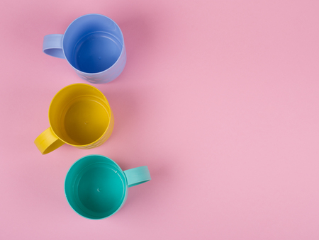 Blue, yellow and green cups in a row on a pastel pink background (minimalism concept, top view), copy space on the right for your textの写真素材